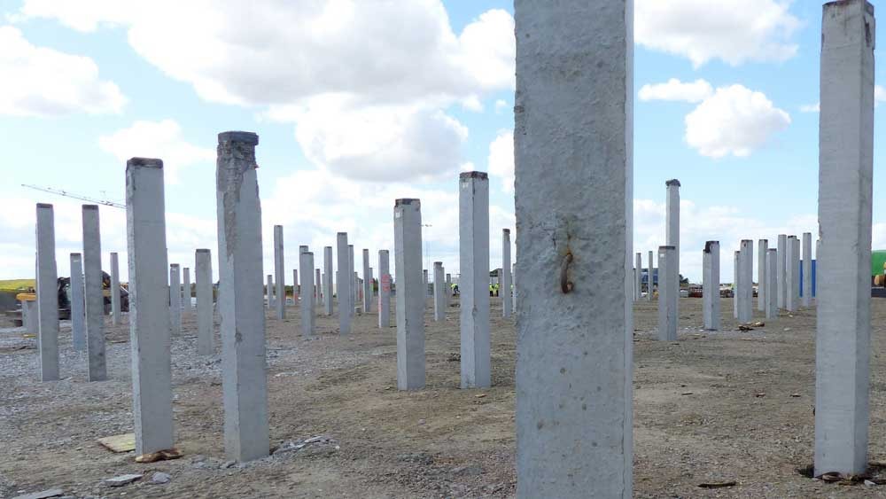 Concrete foundation piles stand upright in a construction site under a cloudy sky.