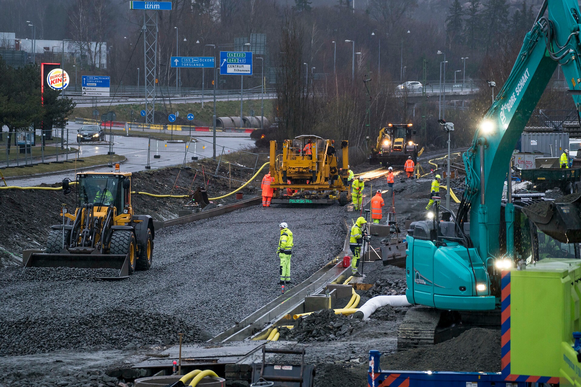 The project includes the section Eriksberg–Pölsebo. Road construction site with heavy machinery and workers in high-visibility clothing.