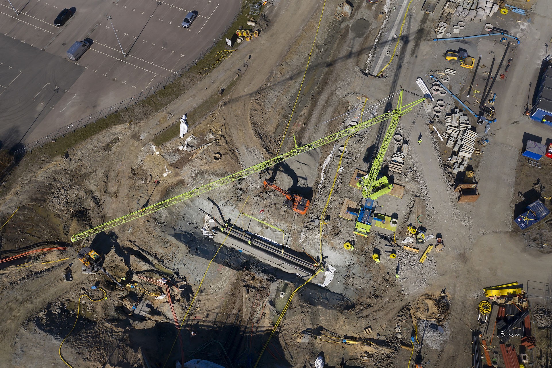 The project will be completed in 2024. Aerial view of a construction site featuring cranes, heavy machinery, and building materials.