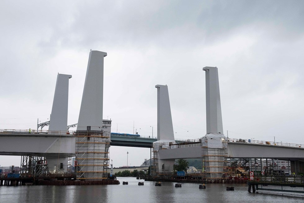 Bridge construction over a river with large vertical supports and scaffolding under a cloudy sky.