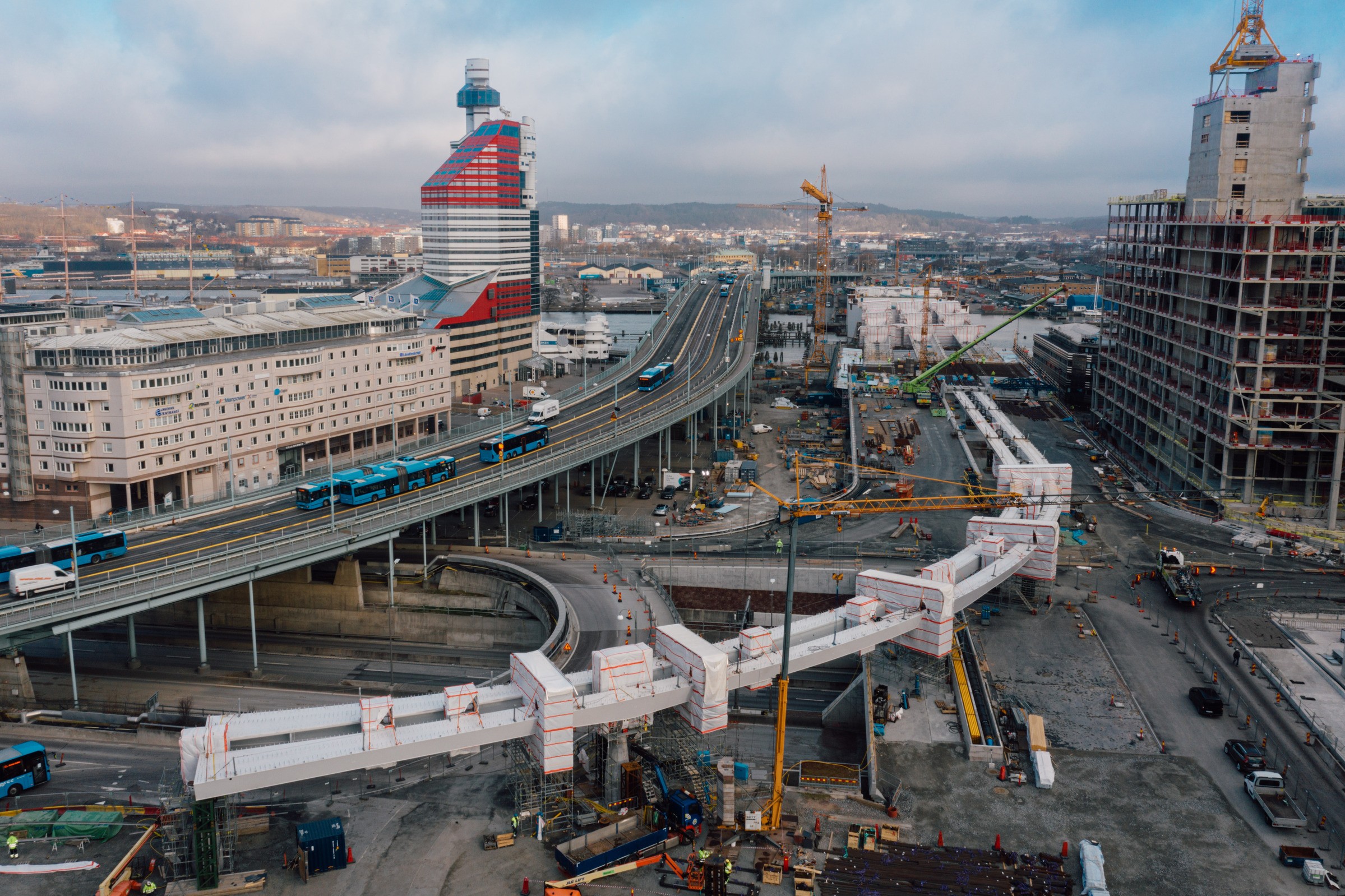 Aerial view of urban construction site with cranes, vehicles, and modern buildings in the cityscape.