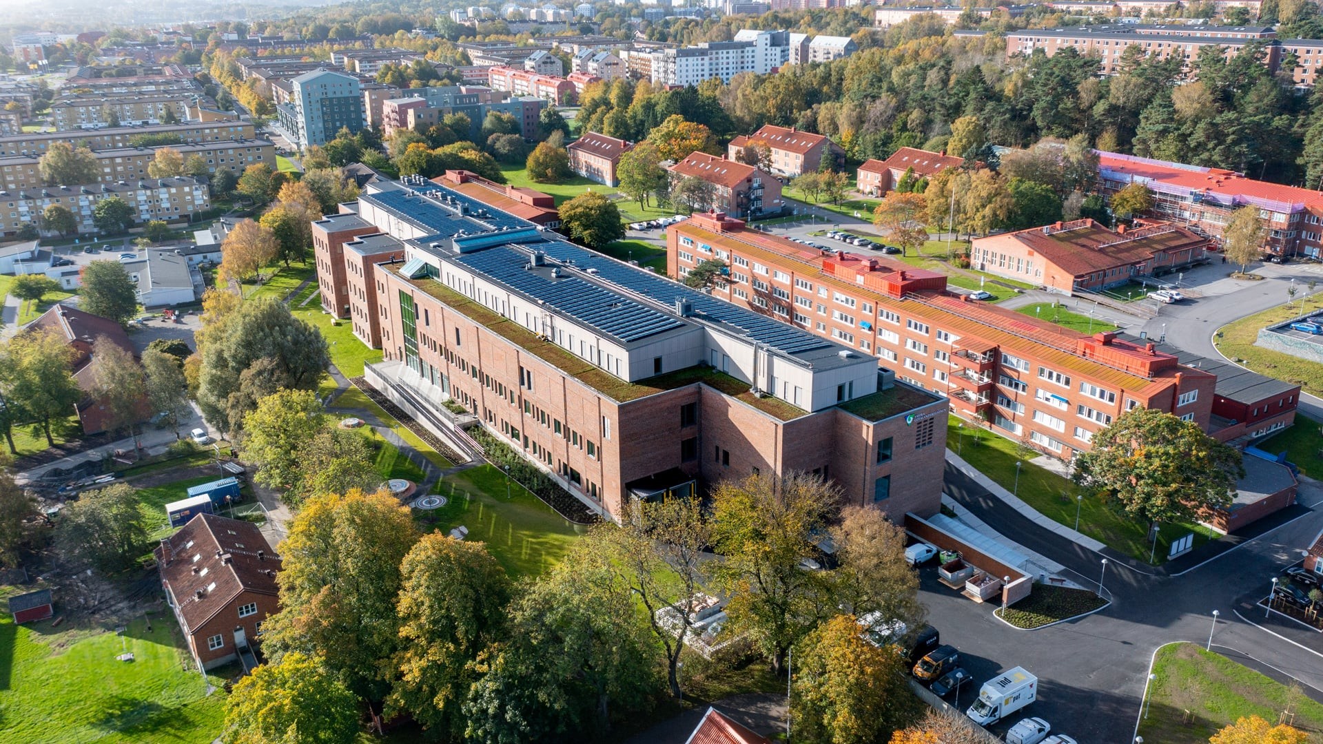 Aerial view of a large brick building surrounded by trees and residential areas in an urban setting.