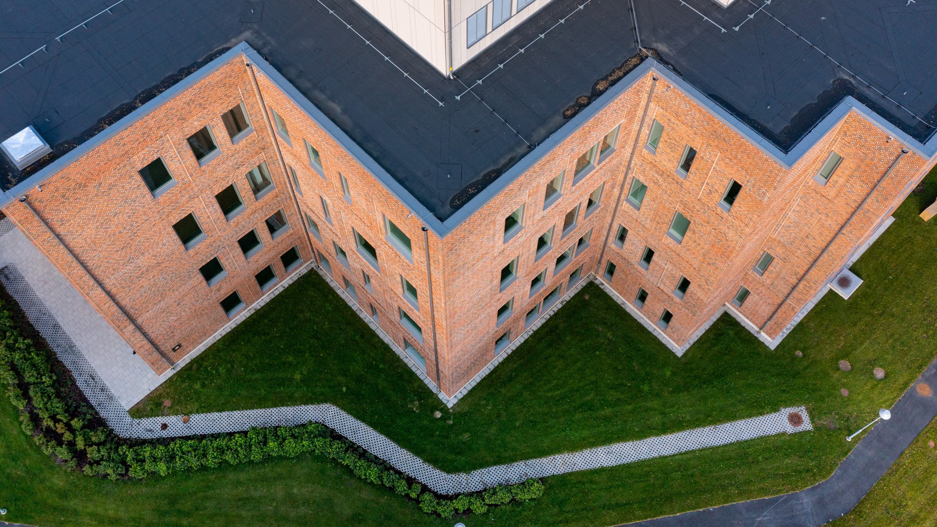 Aerial view of a V-shaped brick building with adjacent green lawn and pathways.
