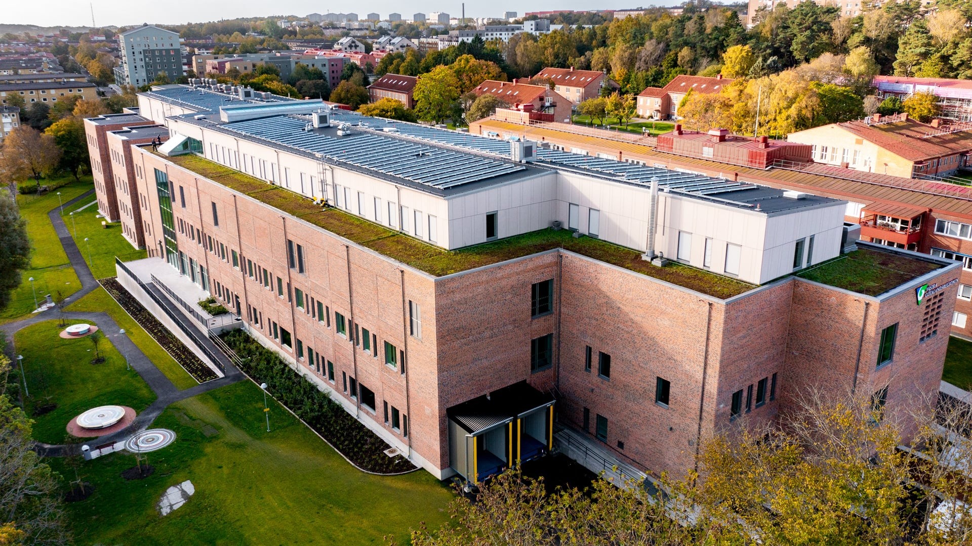 Aerial view of a large, modern brick building with solar panels and green landscaping.