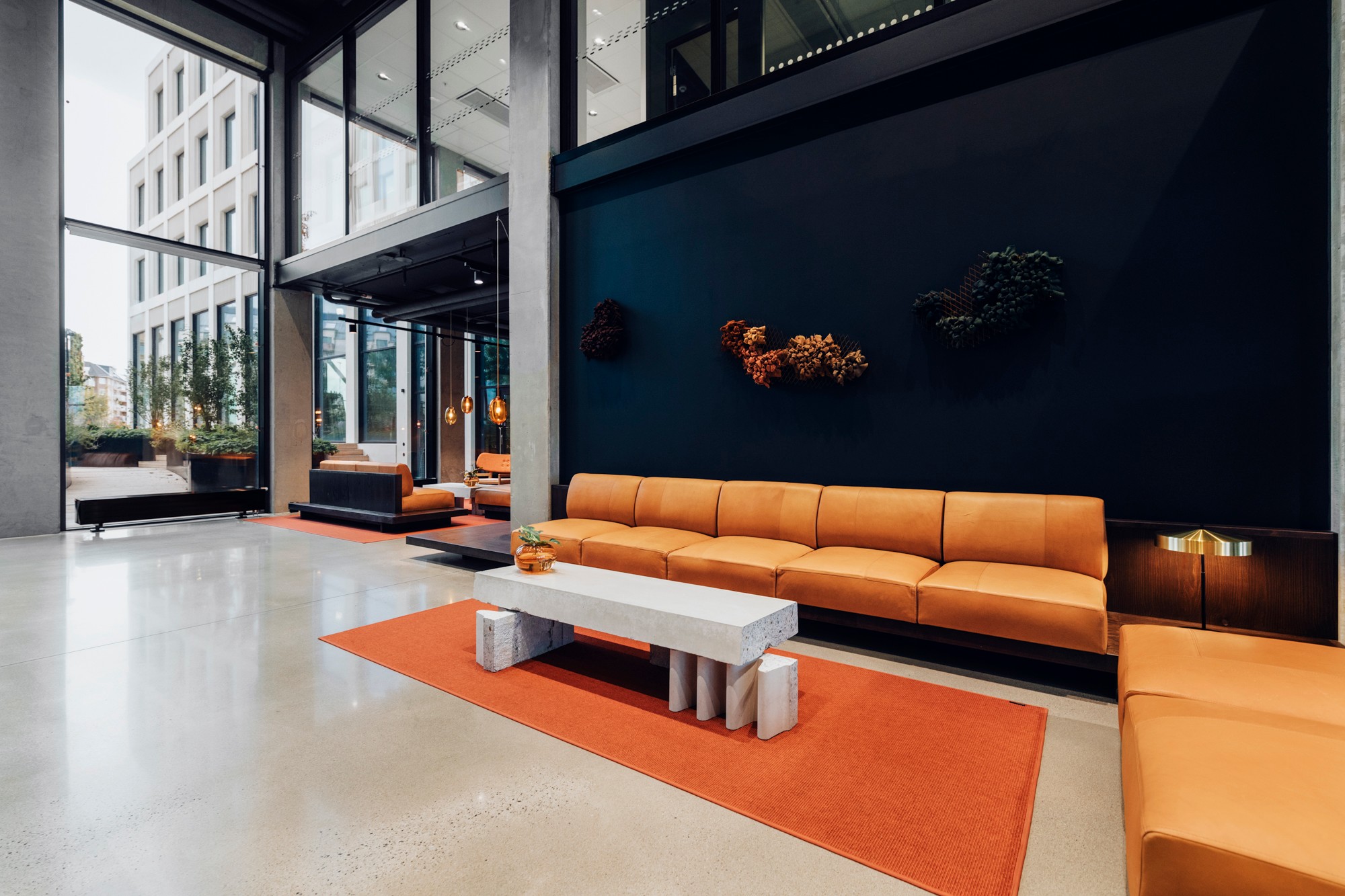 Modern office lounge with orange sofas, concrete table, and large windows.