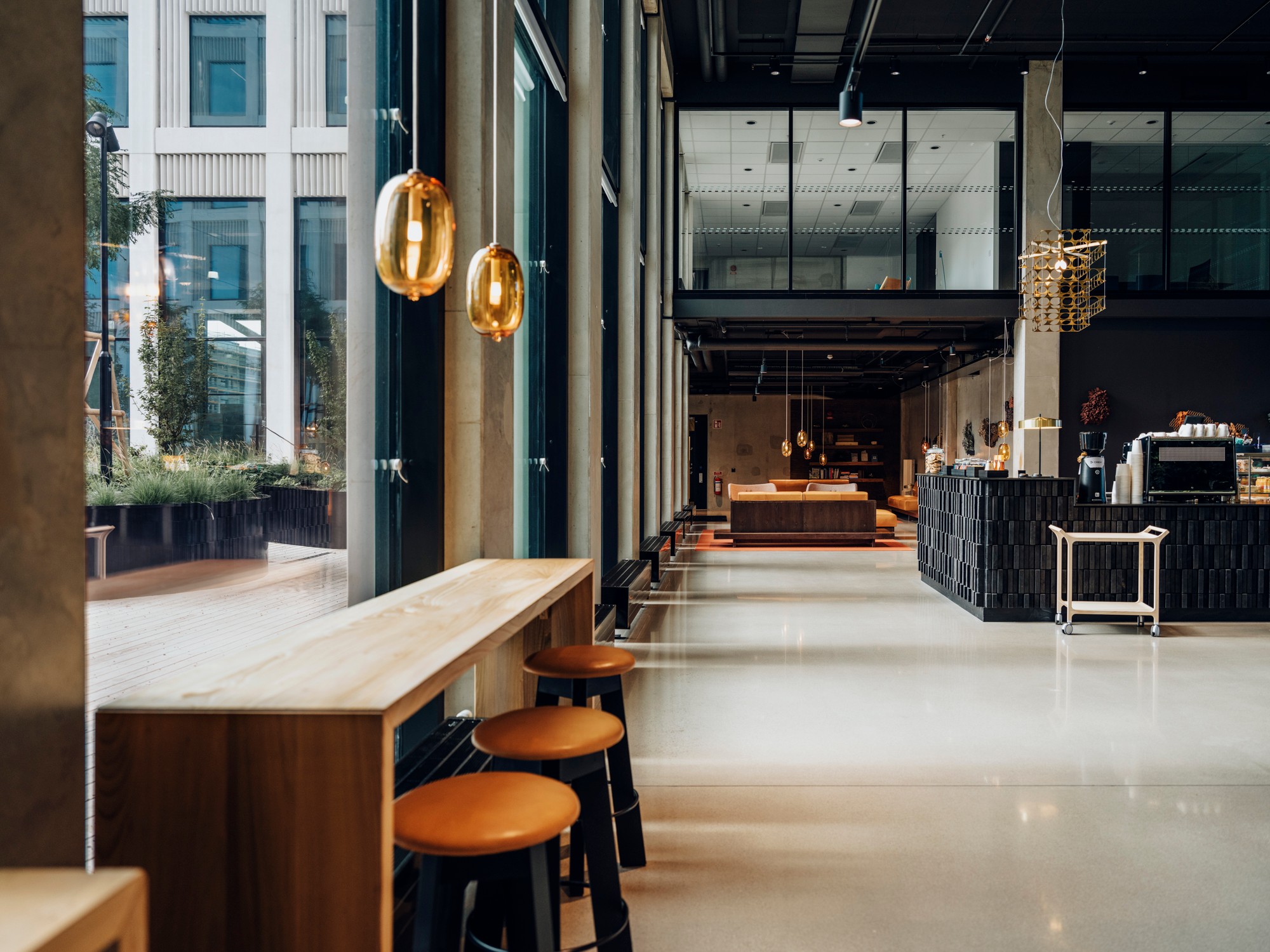 Modern café interior with wooden stools, pendant lights, and large windows.