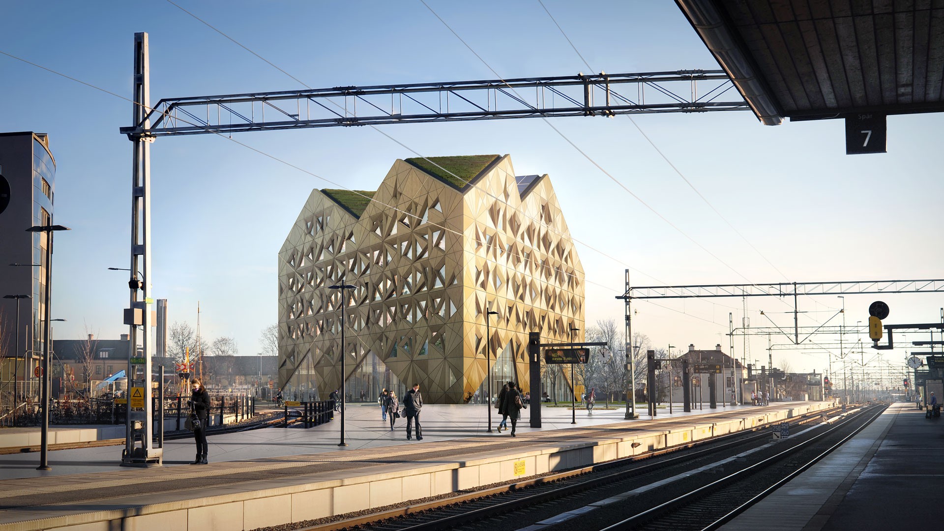 Modern geometric building with green roofs near a train station platform under a clear sky.