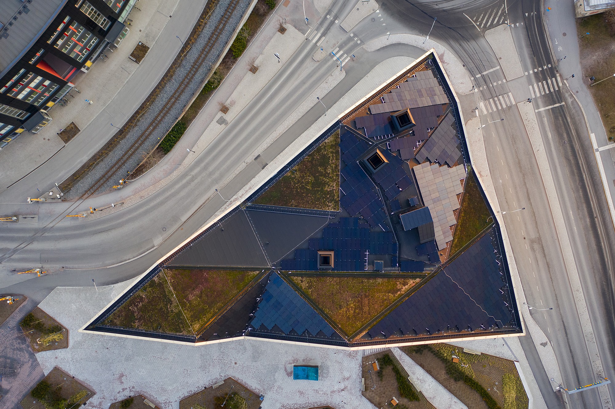 Aerial view of a triangular building with a green roof, surrounded by roads and walkways.