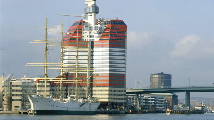 Modern red and white skyscraper beside a docked tall ship in Gothenburg, Sweden's waterfront.