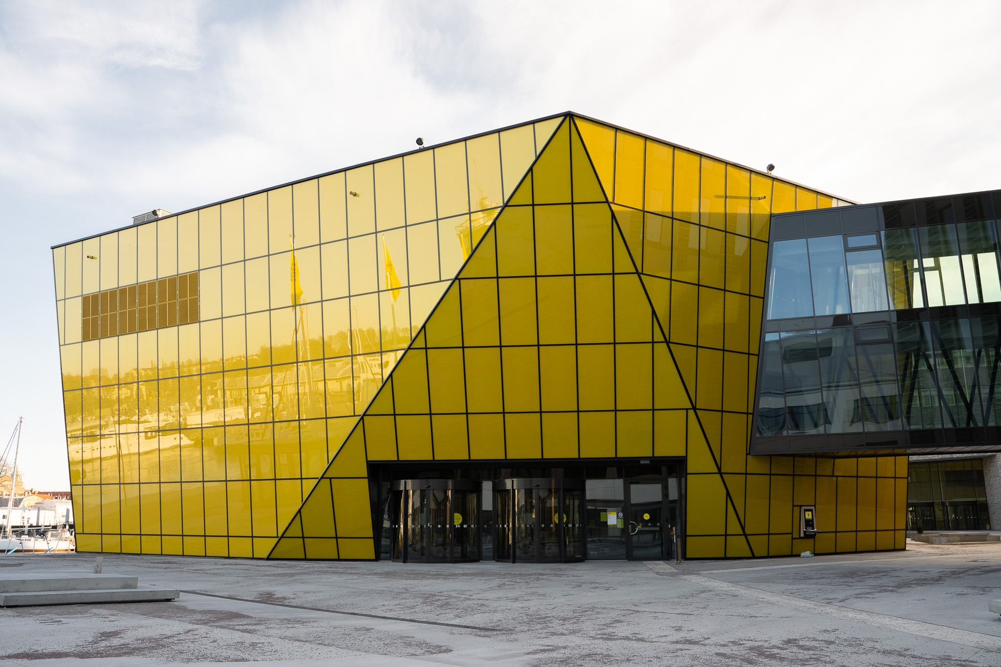 Modernes Gebäude mit auffälliger gelber Glasfassade und geometrischem Design vor blauem Himmel.