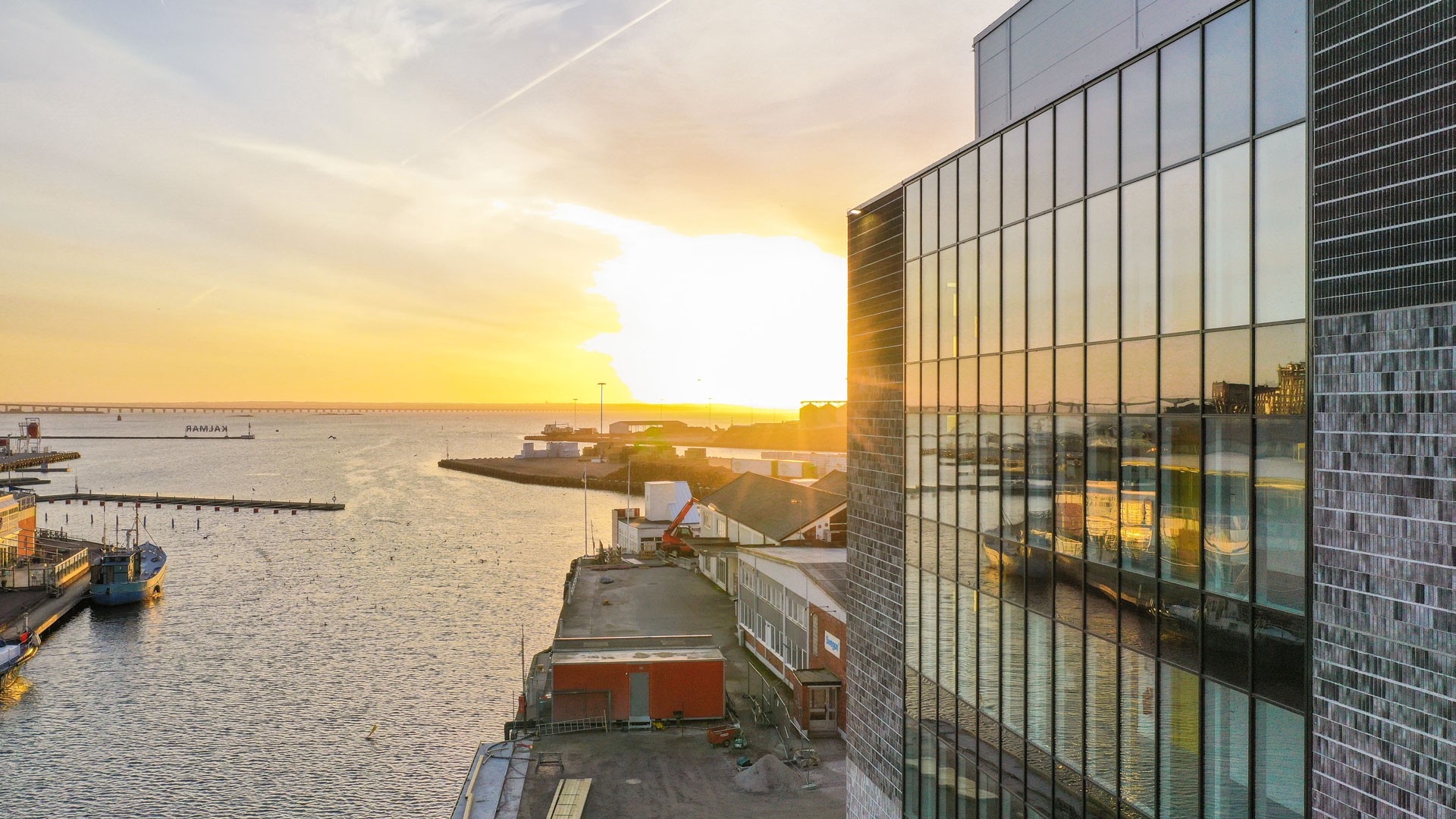 Sunset over a coastal cityscape with modern glass buildings and waterfront docks.