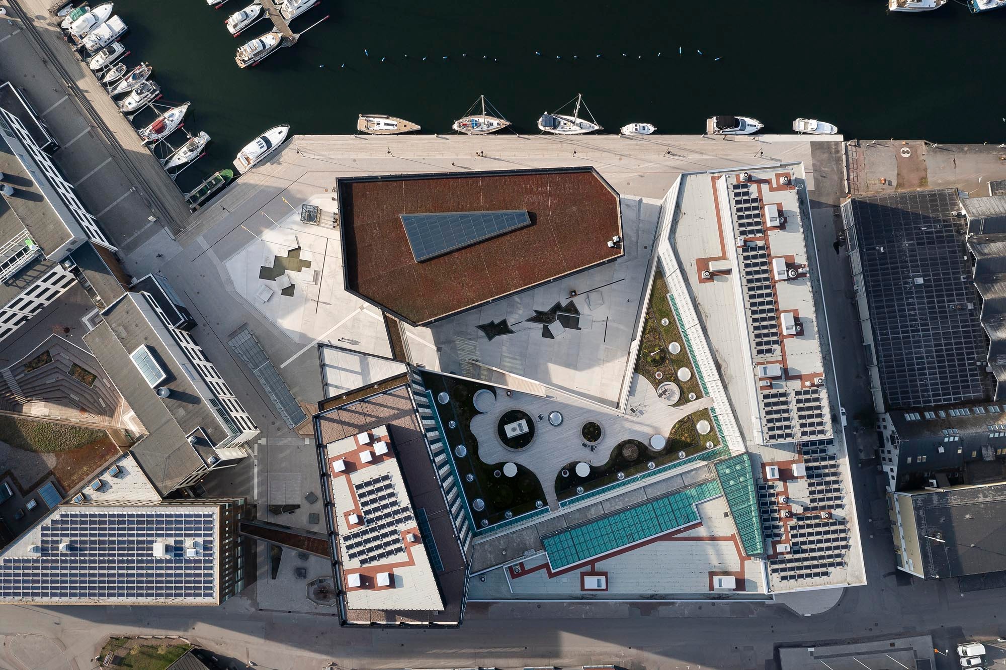 Aerial view of modern waterfront architecture with solar panels and landscaped rooftop areas.