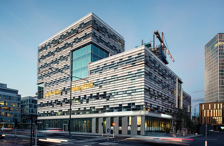 Modern multi-story building with a textured facade and large windows under construction cranes.