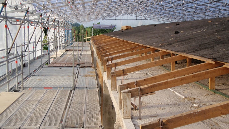 Construction site with scaffolding and roof framework under a protective canopy structure.
