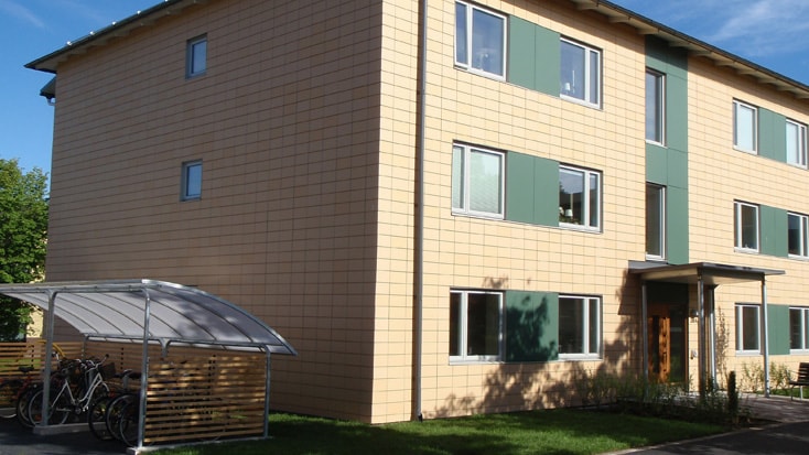 Brogården Modern three-story apartment building with beige facade and green window accents, sunny day.