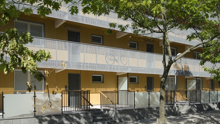 Modern apartment building with yellow facade, trees, and bike motifs on balcony railings.