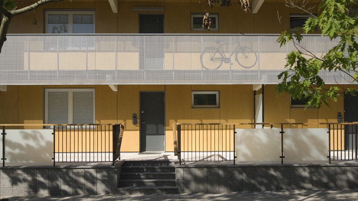 Modern apartment building with yellow facade, metal balcony, and visible parked bicycle.