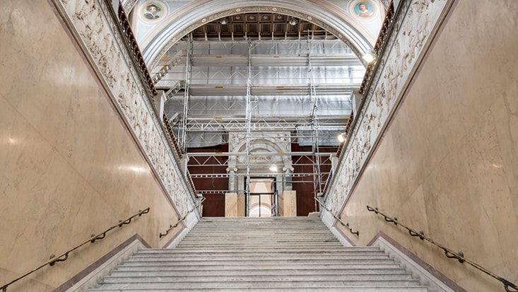 Grand marble staircase under renovation, featuring scaffolding and ornate architectural details.