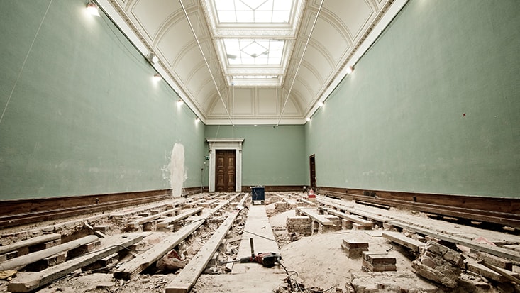 Room under renovation with exposed floor beams, high ceiling, and green walls.