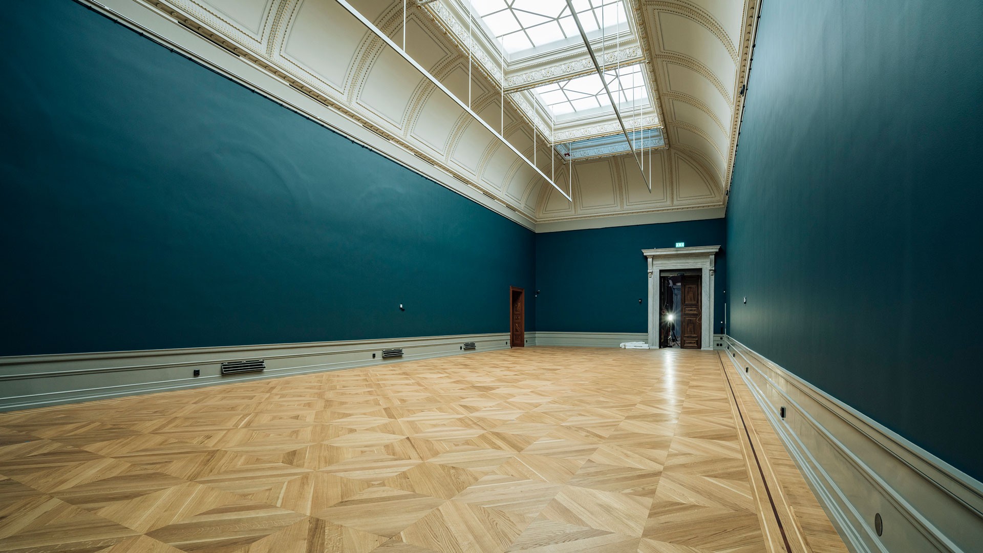 Spacious, elegant room with teal walls, parquet flooring, and a large skylight illuminating the space.