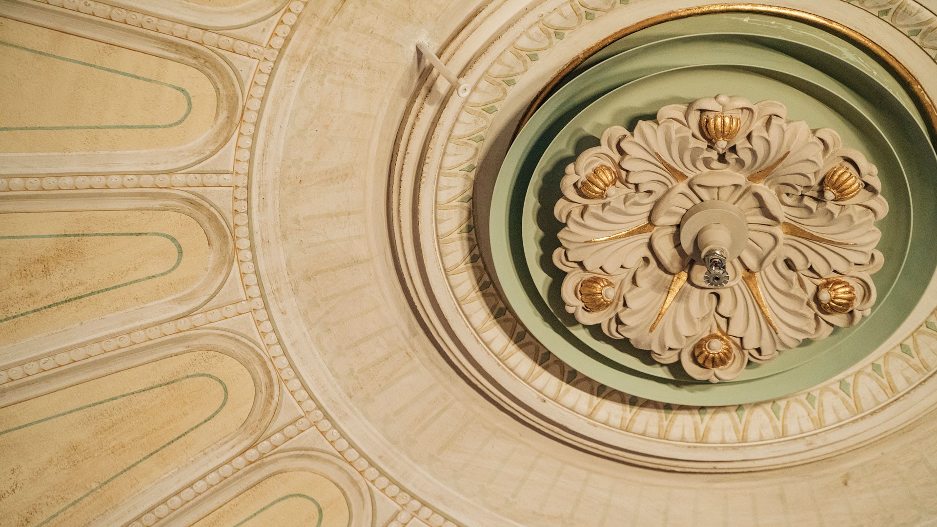 Ornate ceiling design with intricate floral motifs and gold accents on a circular fixture.