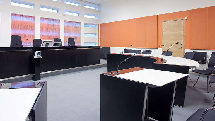 Modern courtroom with black desks, microphones, and orange soundproof panels on the walls.