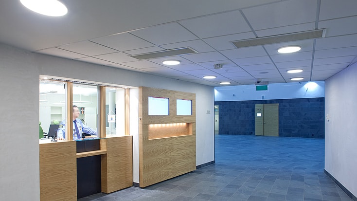 Modern reception area with a security desk, wooden accents, and bright overhead lighting.