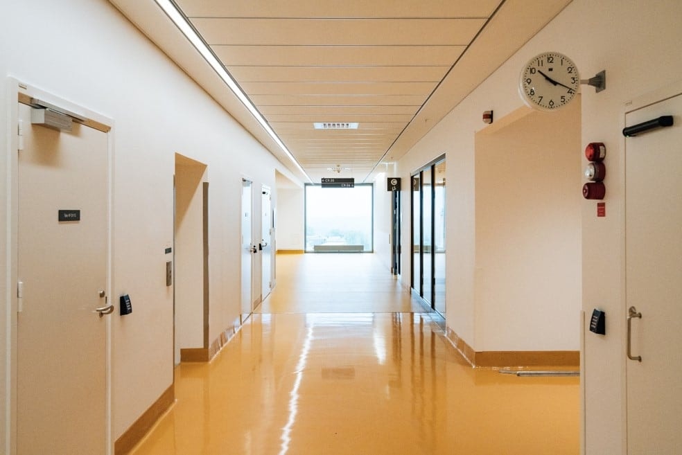 Bright hospital corridor with shiny yellow flooring, white walls, and closed doors on either side.