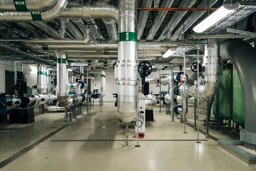 Industrial room with large insulated pipes, valves, and machinery in a utility facility.