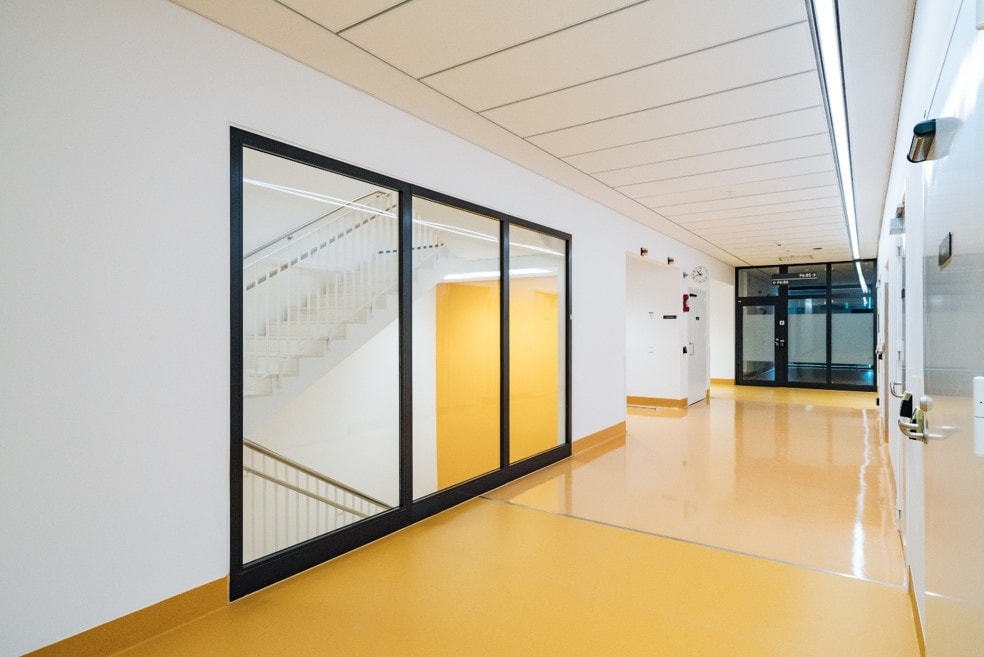 Moderne Diele mit großen Fenstern, gelben Böden und Treppen, die durch das Glas sichtbar sind.
