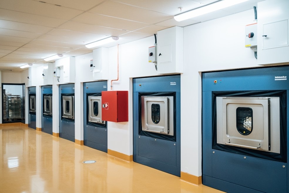 A row of industrial laundry machines in a clean, well-lit facility with a modern design.