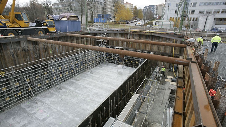 Construction site with a large concrete foundation, steel beams, and workers in safety gear.