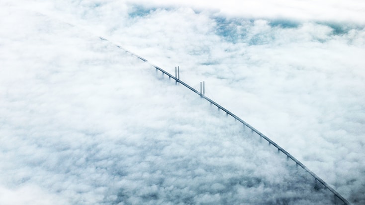 The Öresund Bridge Aerial view of a bridge partially obscured by clouds, showcasing its towering structure against the sky.