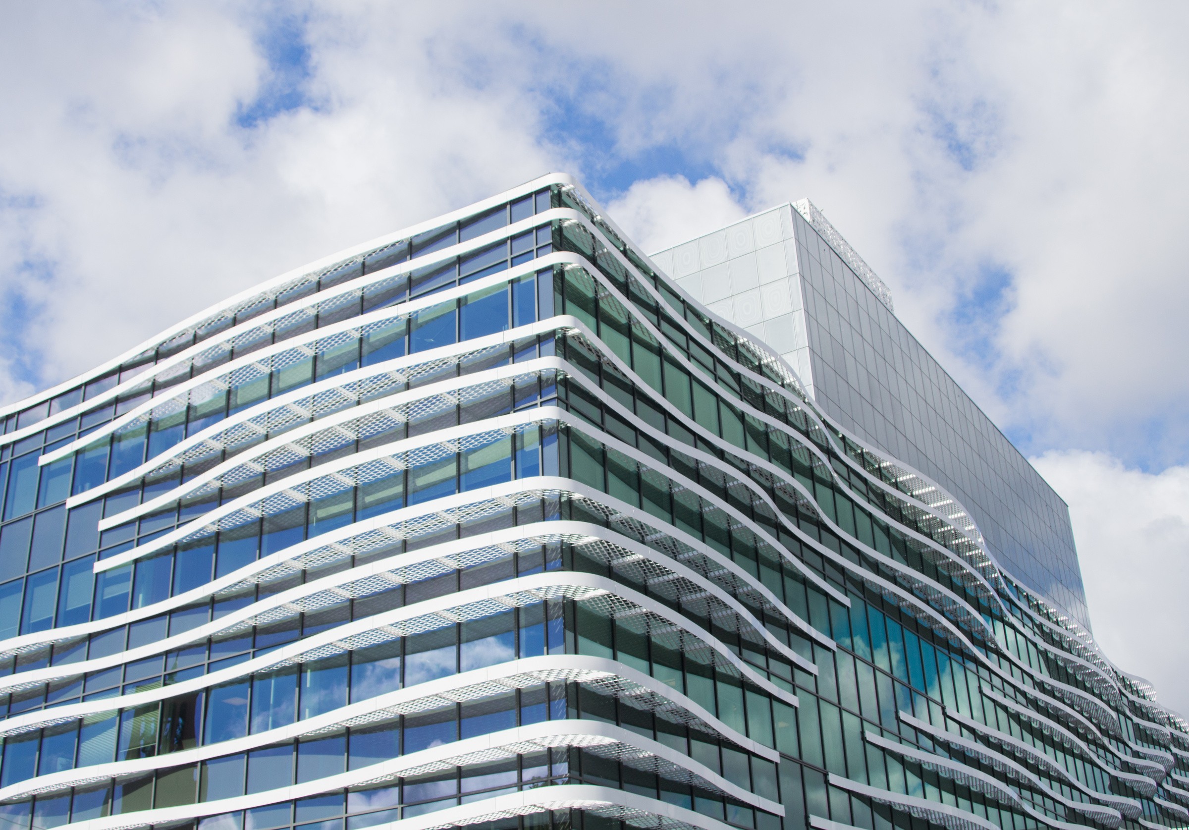 Modern glass building with unique wave-like white architectural elements against a blue sky.