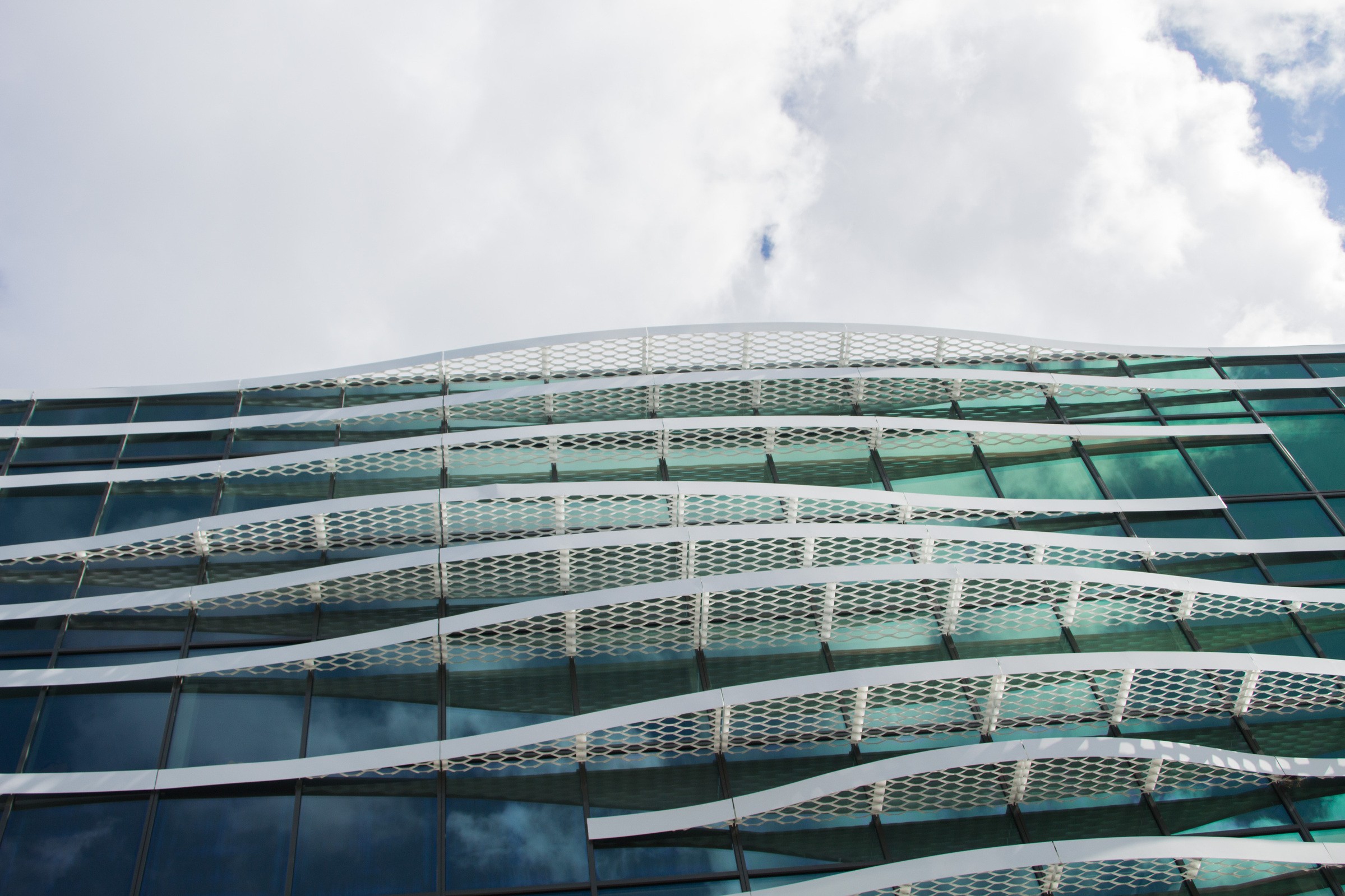 Modern building facade with wavy, white lattice design against a cloudy sky backdrop.