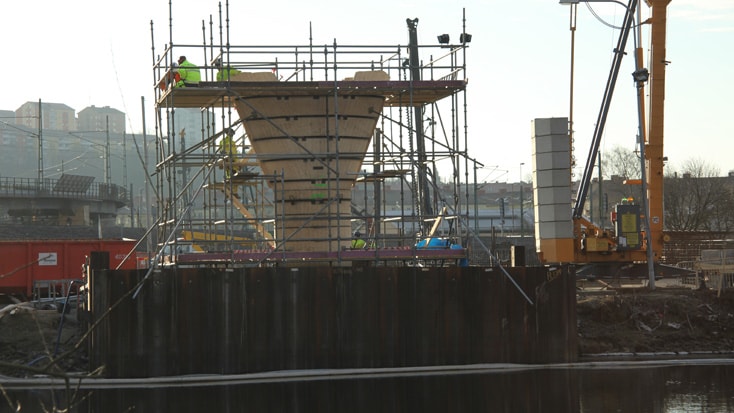 Partihallsförbindelsen Bridge Construction site with scaffolding around a concrete structure, crane, and urban background.