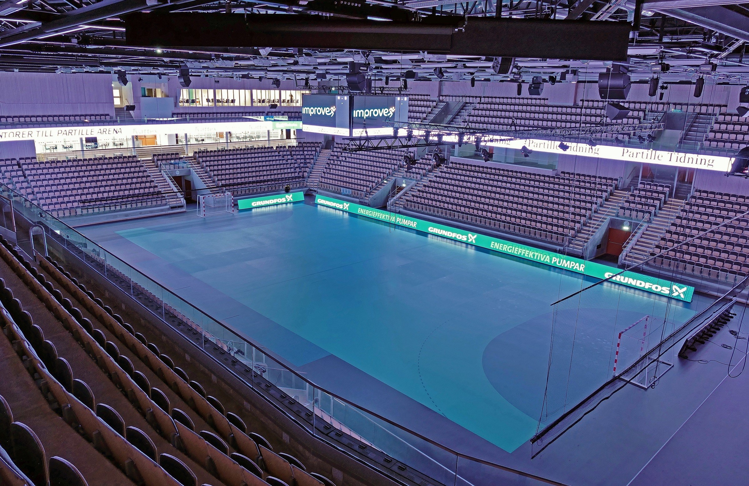 Indoor sports arena with empty seating and a blue playing surface, ready for events.