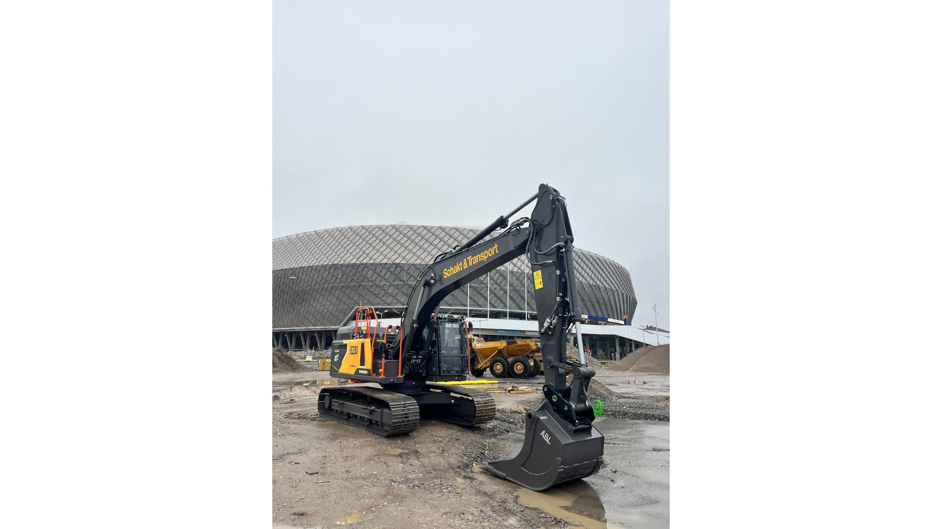 Electric band excavator in production in the Slakthusområdet. An excavator is working at a construction site in front of a large arena.