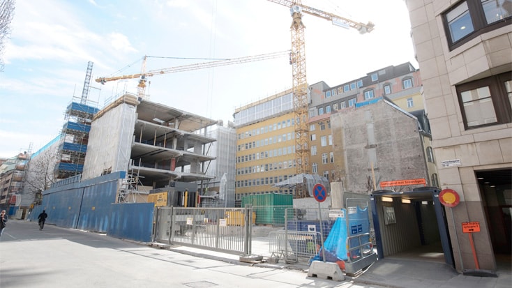 Urban construction site with cranes, scaffolding, and partially built structures under clear sky.