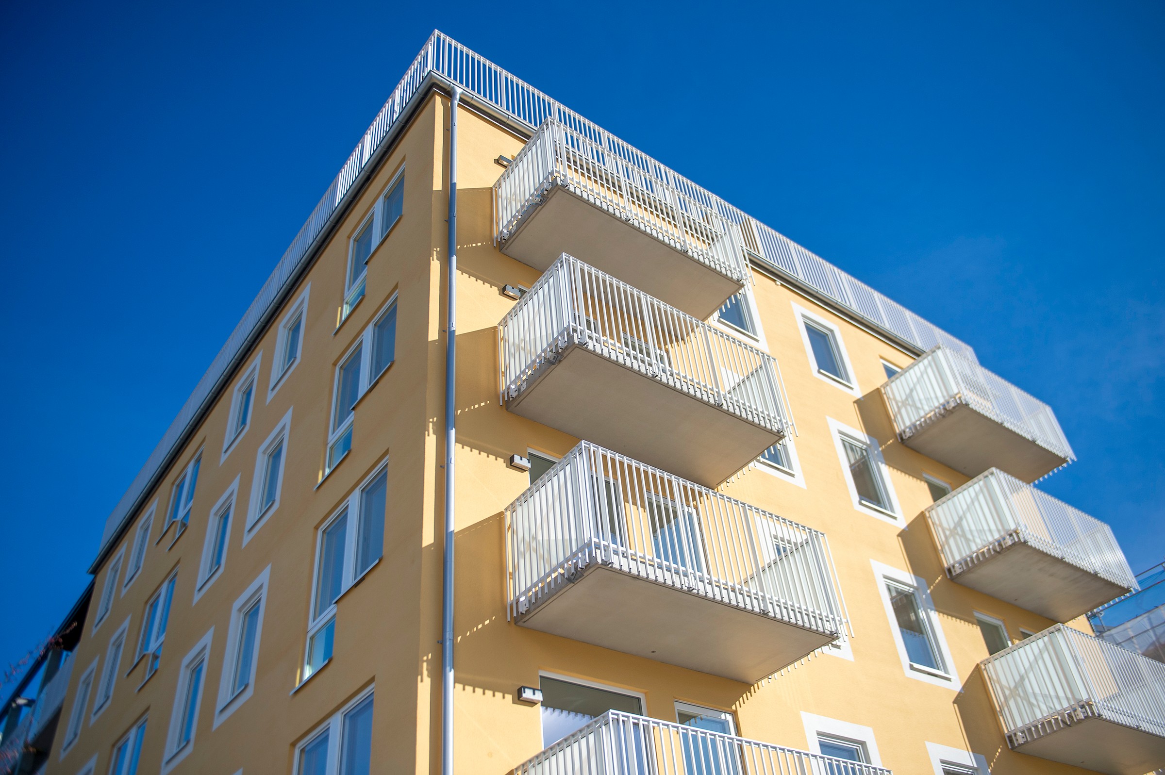 Skanska's condominium block Klövern in Täby Park. Modern yellow apartment building with multiple balconies against a clear blue sky.