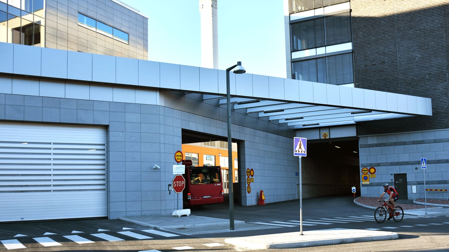 Fredriksdal bus depot roof Modern urban entrance with pedestrian crosswalk, cyclist, bus, and stop sign under a sleek canopy.