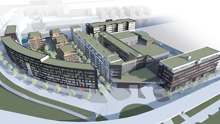 Since bus depot is located centrally, buses will be able to travel smoothly to and from the depot. Aerial view of a modern, multi-building complex with green rooftops and landscaped surroundings.