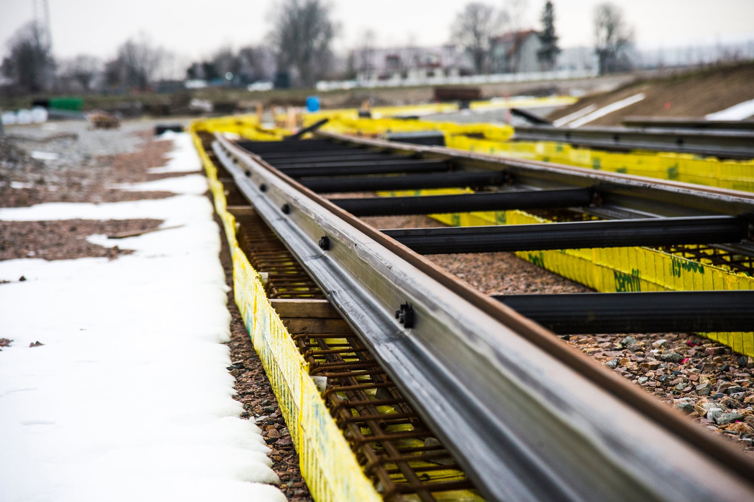Close-up of railway tracks under construction, surrounded by yellow safety barriers and snow.