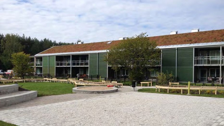 Modernes grünes Gebäude mit einem grasbedeckten Dach, umgeben von einem angelegten Innenhof und Bänken.