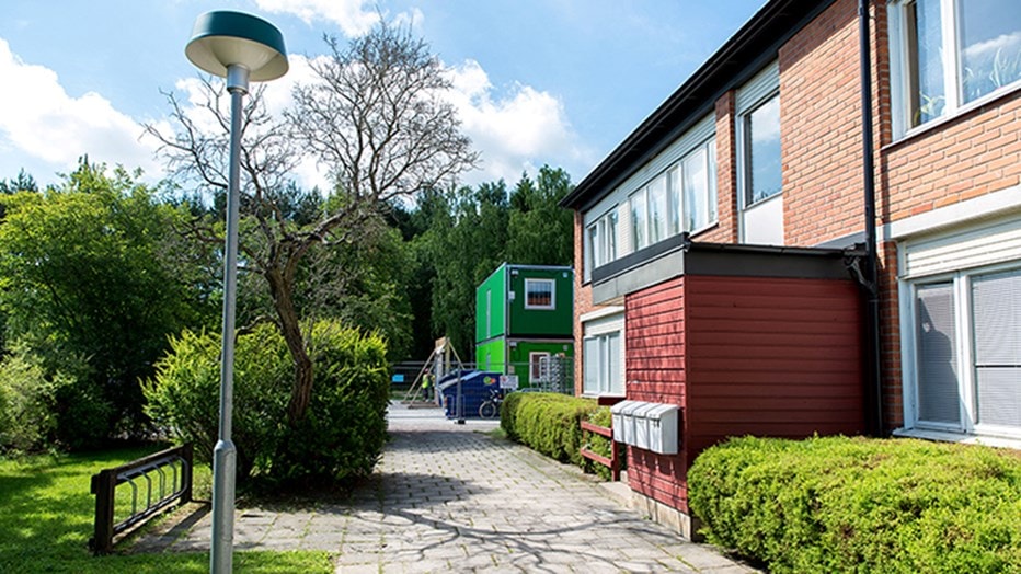 Residential area with modern buildings, a green container, pathway, and lush greenery.