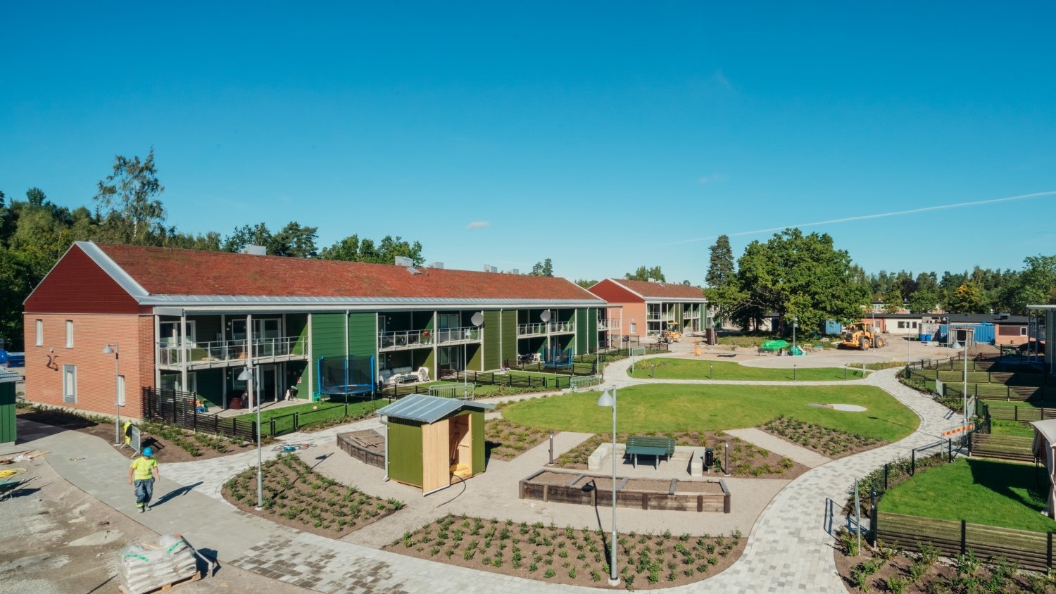 Modernes Wohnkomplex mit angelegtem Garten, mit roten und grünen Gebäuden unter blauem Himmel.
