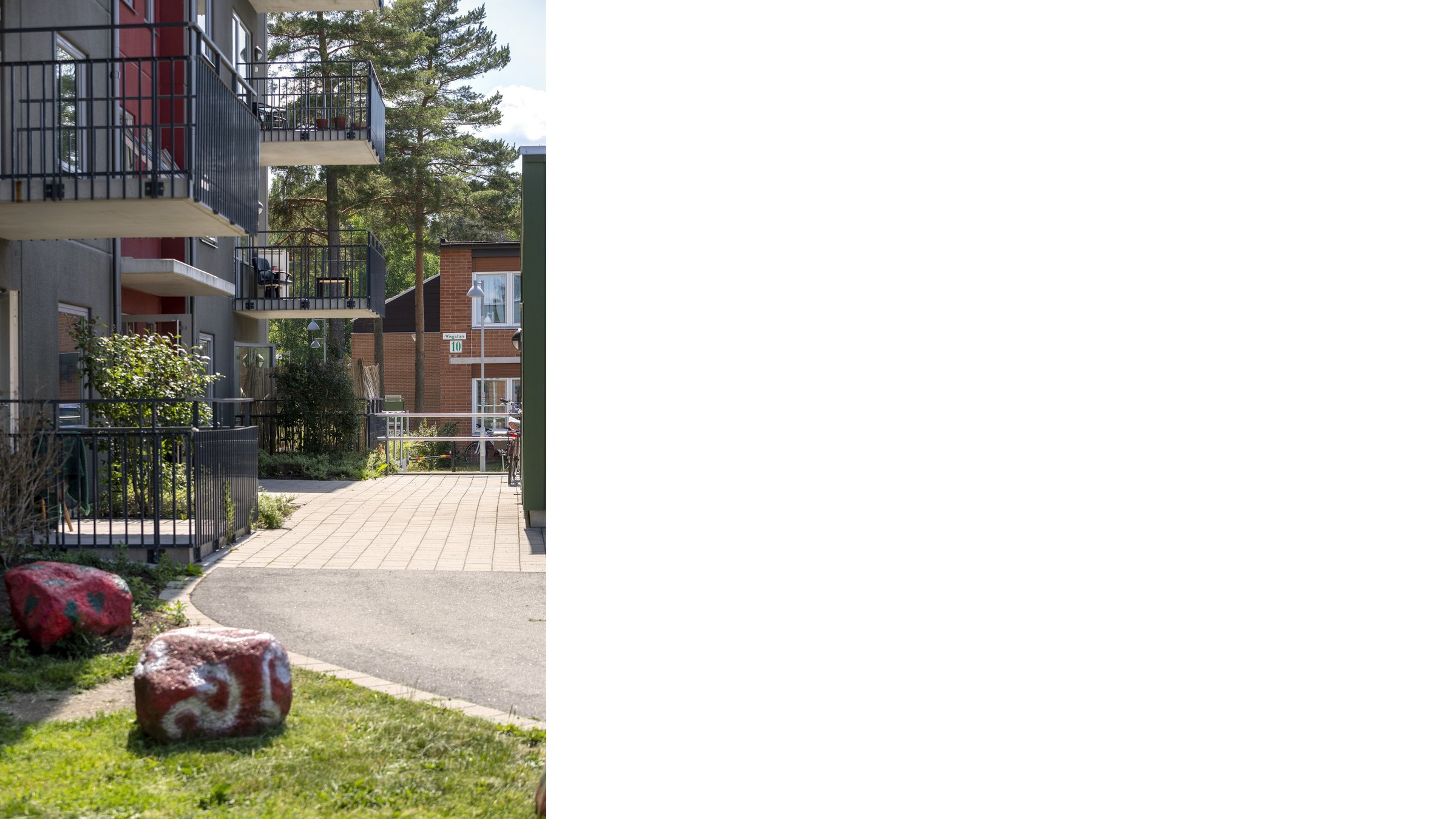 Apartment building with balconies, pathway, and painted rocks in a grassy area under trees.