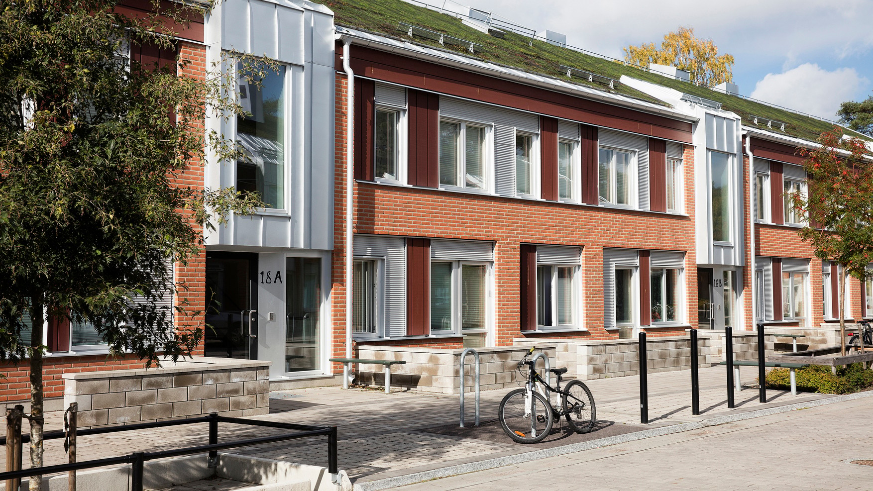 Modern brick building with green roof, large windows, and bike racks, under a clear sky.