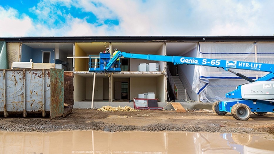 Construction site with a Genie S-65 lift, exposed building interiors, and muddy ground.