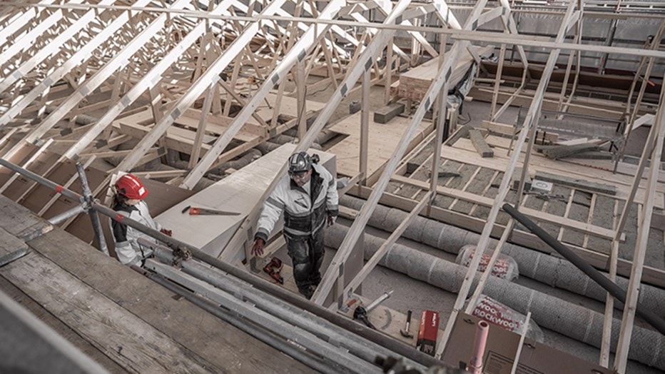 Construction workers in protective gear working on a wooden roof frame with scaffolding.